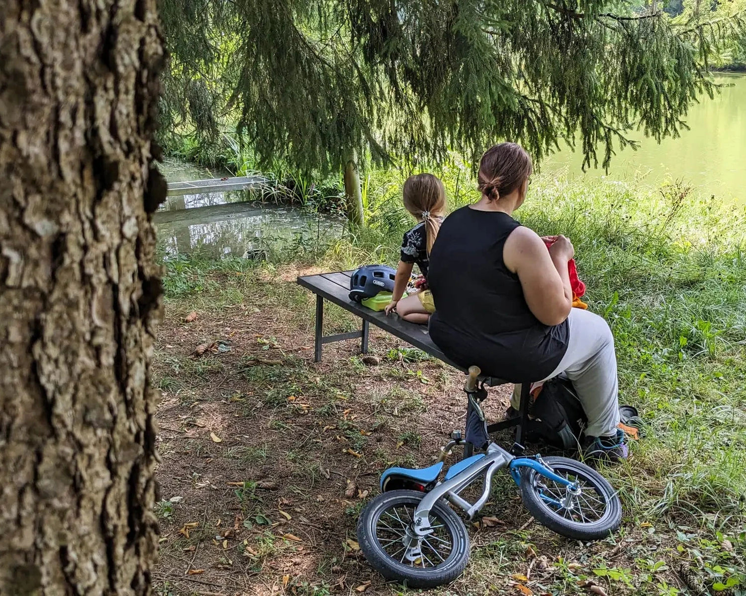 Frau strickt in der Natur mit handgefärbter Wolle. Neben ihr sitzt ihr Sohn auf einer Bank und beobachtet die Natur.